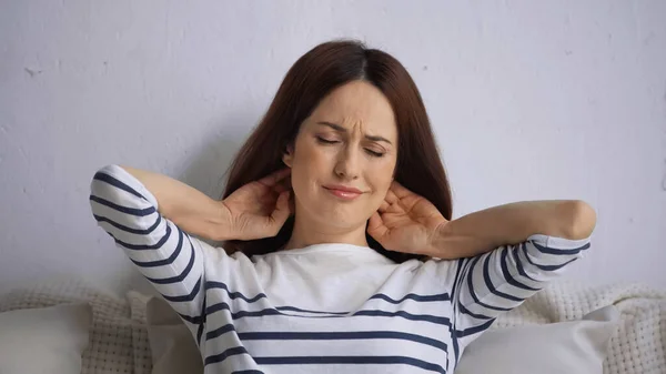 Brunette woman with closed eyes frowning while feeling pain in neck — Stock Photo