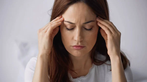 Brunette woman with closed eyes touching head while suffering from migraine on grey background — Stock Photo