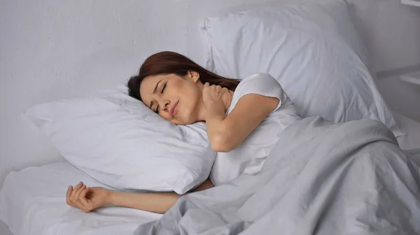 Brunette woman lying on bed with closed eyes and touching painful neck — Stock Photo