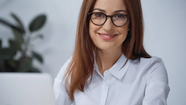 Весела бізнес-леді в окулярах посміхається на камеру в офісі — стокове фото