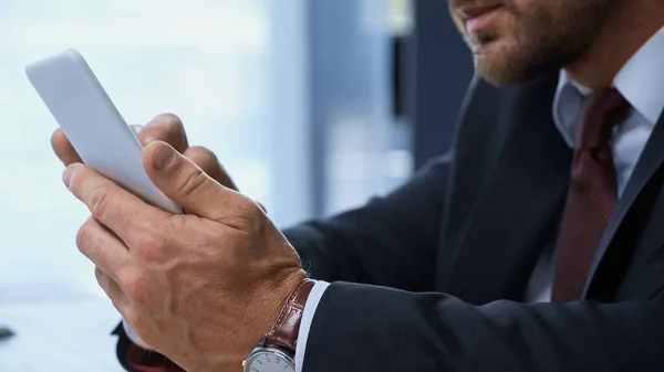 Vista parcial de la mensajería de hombre de negocios en el teléfono móvil en la oficina - foto de stock