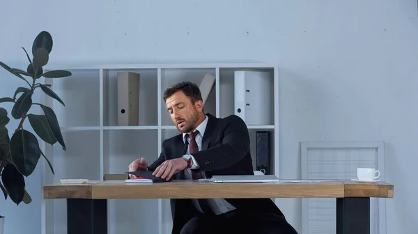 Hombre de negocios en traje portátil de apertura mientras está sentado en el escritorio - foto de stock