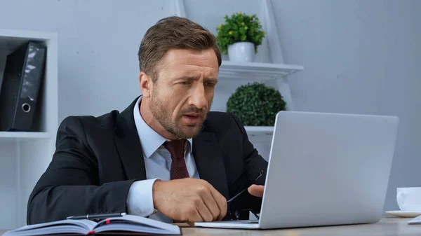 Nachdenklicher Geschäftsmann schaut im Büro auf Laptop — Stockfoto