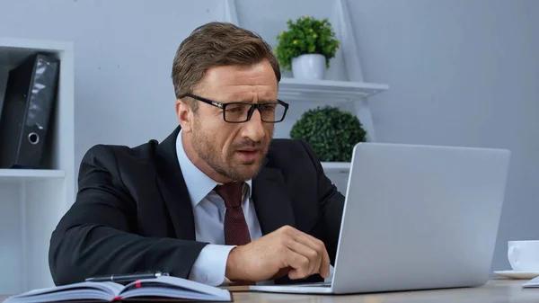 Concentrated businessman in eyeglasses working at laptop in office — Stock Photo