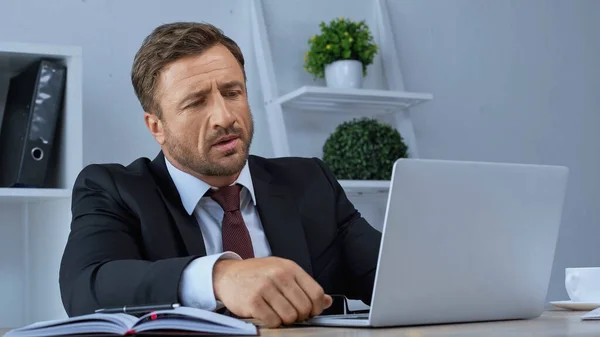 Homem de negócios pensativo olhando para laptop enquanto trabalhava no escritório — Fotografia de Stock