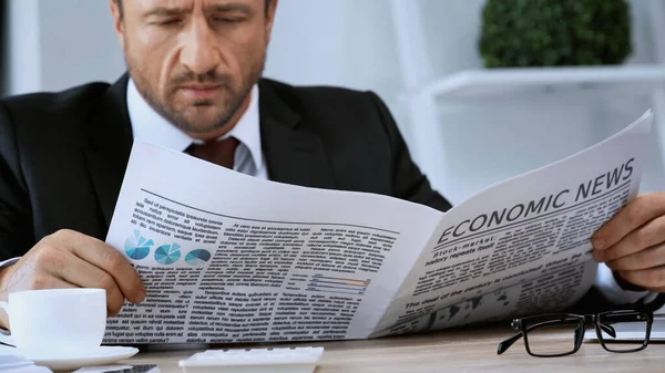 Blurred businessman reading newspaper near eyeglasses and calculator on work desk — Stock Photo