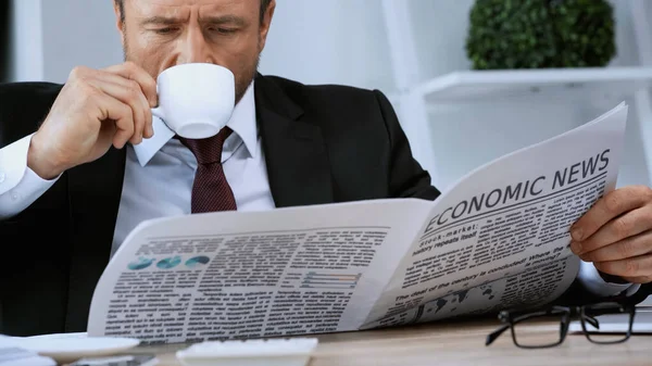 Бизнесмен пьет кофе и читает экономические новости в офисе — стоковое фото