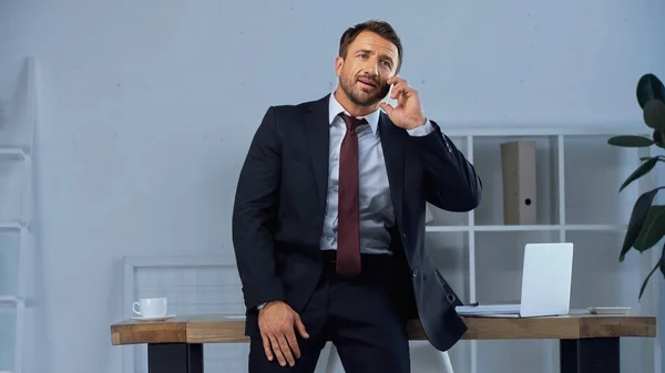 Людина в офіційному одязі говорить на мобільному телефоні, стоячи на робочому місці в офісі — стокове фото