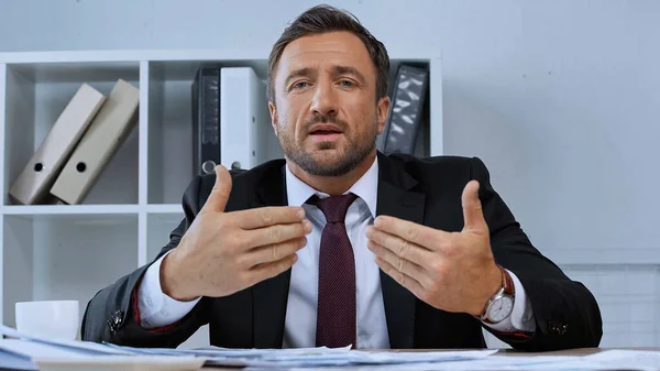 Hombre en el gesto de desgaste formal mientras habla en la cámara en la oficina - foto de stock