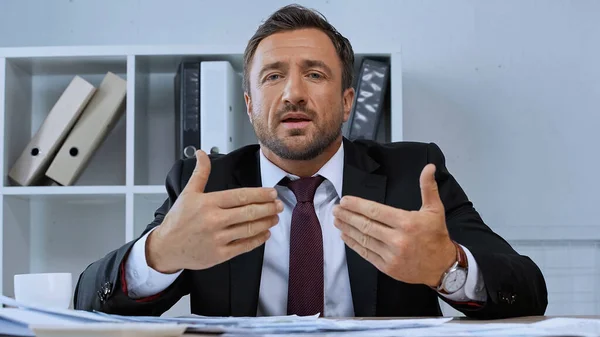 Man in formal wear gesturing while talking at camera in office — Stock Photo