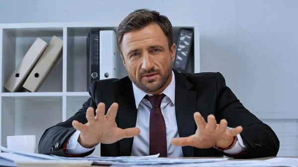 Businessman in suit gesturing and looking at camera in office — Stock Photo