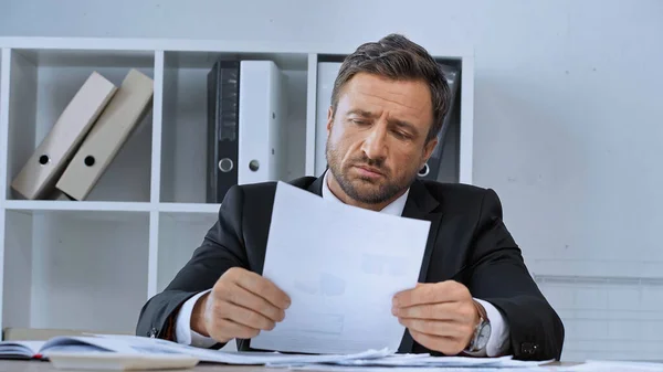Homem de negócios chateado olhando para o documento enquanto trabalhava no escritório — Fotografia de Stock