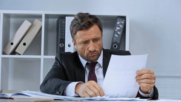 Displeased businessman working with papers at work desk in office — Stock Photo