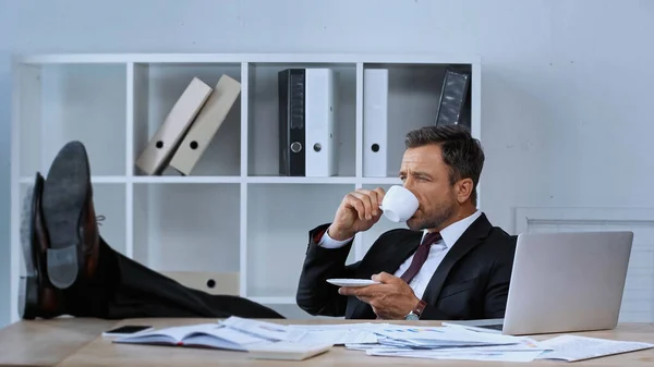 Бизнесмен, сидящий с ногами на столе во время перерыва на кофе в офисе — стоковое фото