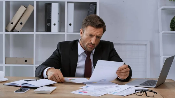 Mann in offizieller Kleidung arbeitet mit Dokumenten in der Nähe von Laptop am Arbeitsplatz — Stockfoto