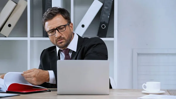 Seriöser Geschäftsmann mit Brille, der im Büro mit Notebook und Laptop arbeitet — Stockfoto