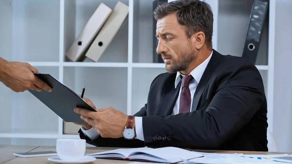 Geschäftsmann signiert Dokument auf Klemmbrett in den Händen von Assistent — Stockfoto