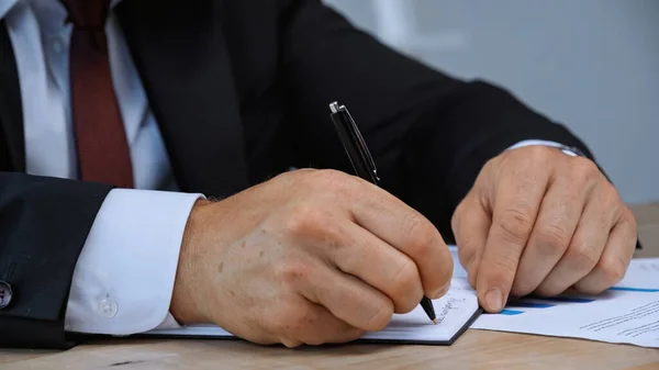 Обрезанный взгляд бизнесмена, пишущего ручкой в блокноте — стоковое фото