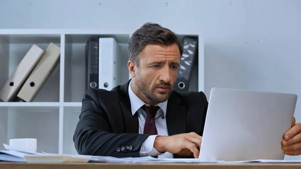 Hombre de negocios en blazer negro escribiendo en el ordenador portátil mientras trabaja en la oficina - foto de stock