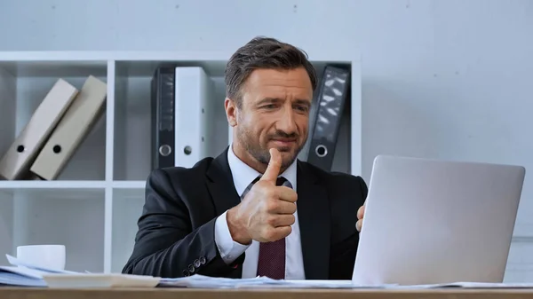 Sonriente hombre de negocios mostrando el pulgar hacia arriba durante la videollamada en el ordenador portátil - foto de stock