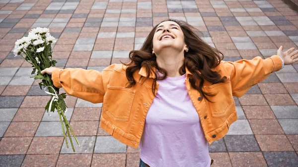 High angle view of happy woman holding white flowers and standing with outstretched hands — Fotografia de Stock