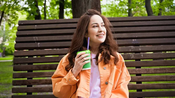 Счастливая женщина, держа в руках кофе, пойдет с соломинкой в парк — стоковое фото