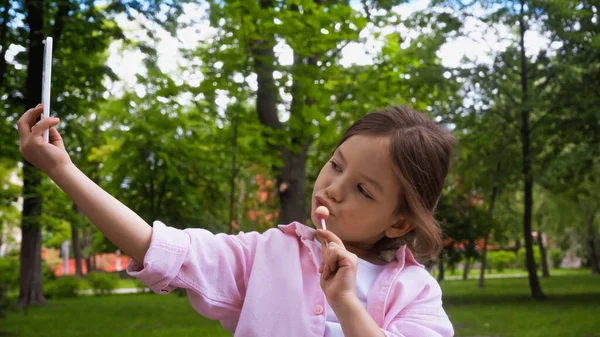 Kind hält Lutscher am Stock und macht Selfie mit Smartphone im Park — Stockfoto