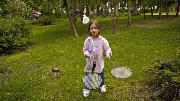 Kid in casual clothing playing badminton on green grass in park — Stock Photo