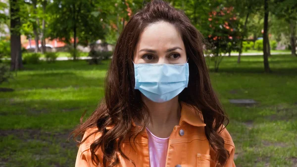 Woman in blue medical mask looking away in green park — Stock Photo