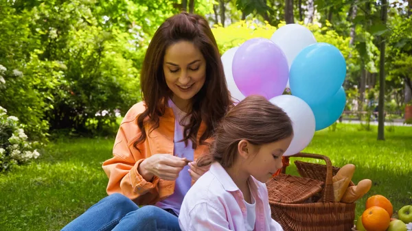 Щаслива мати плете волосся дочки біля повітряних куль в парку — стокове фото