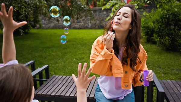 Mother blowing soap bubbles near cute daughter in park — Stock Photo