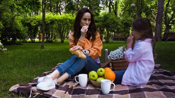Madre e hijo comiendo baguette fresca durante el picnic en el parque - foto de stock