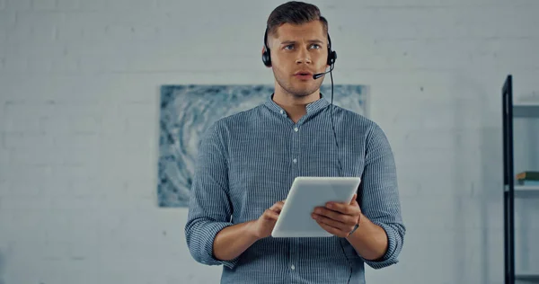 Teleworker in headset with microphone talking and holding digital tablet - foto de stock