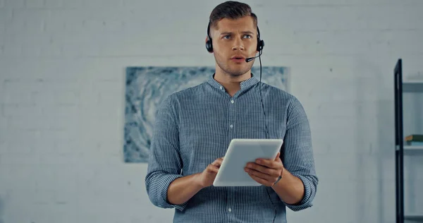 Télétravailleur dans casque avec microphone parlant et tenant tablette numérique — Photo de stock