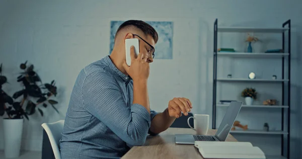 Side view of man in glasses talking on mobile phone while working remotely at home — Foto stock