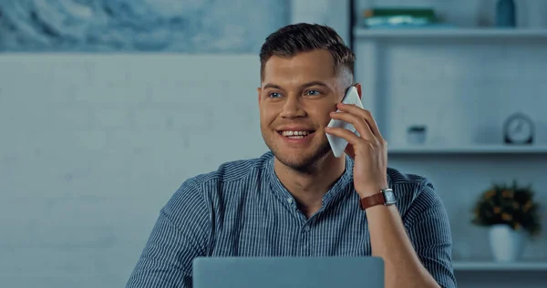 Happy man in glasses talking on smartphone while working remotely at home — Stock Photo