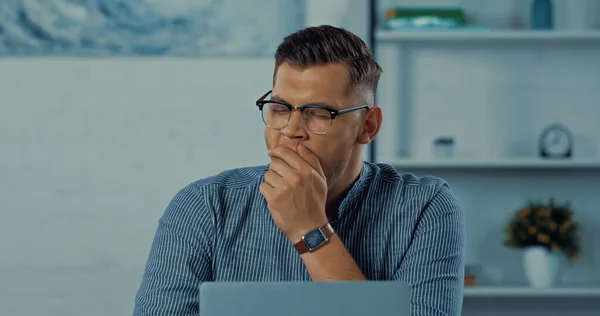 Tired freelancer in glasses yawning near laptop while working from home — Stock Photo