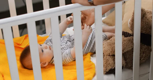 Father holding hand of infant boy in baby crib — Stock Photo