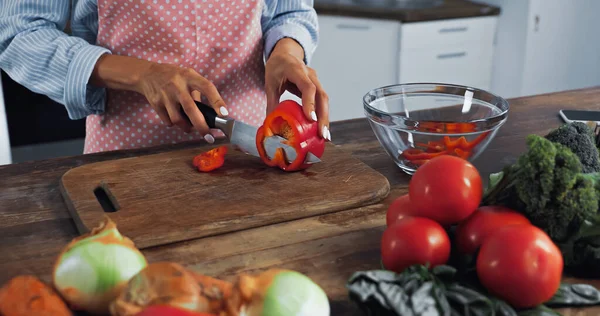 Vue recadrée de la femme coupant le poivron près du bol et différents légumes sur le plan de travail — Photo de stock