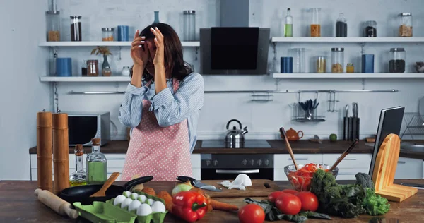 Woman wiping irritated eyes near chopped onion on chopping board — Foto stock