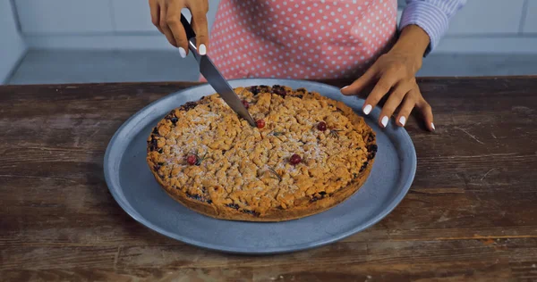 Cropped view of woman cutting baked pie on tray in kitchen — Stock Photo