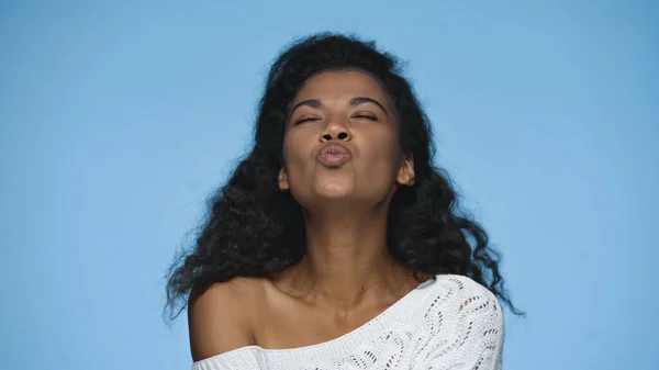 Happy african american woman pouting lips and sending air kiss isolated on blue - foto de stock