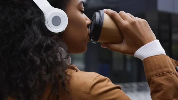 Happy african american woman in headphones drinking coffee to go on street - foto de stock