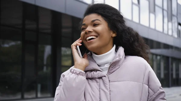 Happy african american woman in puffer jacket talking on smartphone outside — Photo de stock
