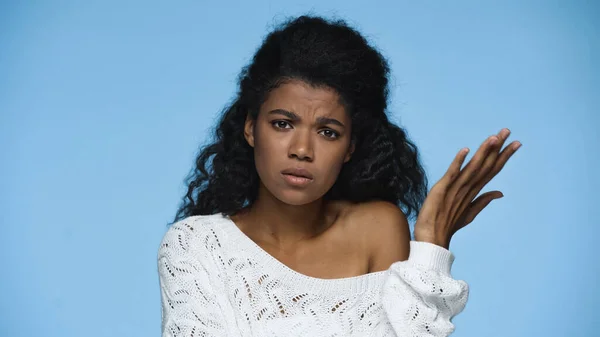 Displeased african american woman in white knitted sweater gesturing isolated on blue — Stockfoto