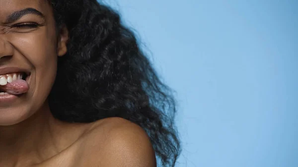 Cropped view of brunette african american woman sticking out tongue isolated on blue — Stock Photo