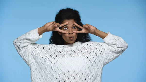 African american woman in white knitted sweater pouting lips and showing peace sign isolated on blue — Stockfoto