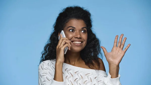 Gioiosa donna afroamericana in maglione bianco lavorato a maglia che parla su smartphone isolato su blu — Foto stock
