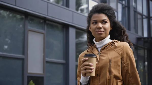 Young african american woman holding coffee to go on urban street - foto de stock