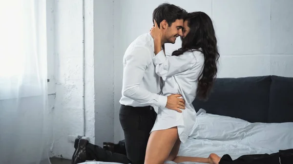 Happy businessman in white shirt hugging and kissing cheerful woman in bedroom — стоковое фото